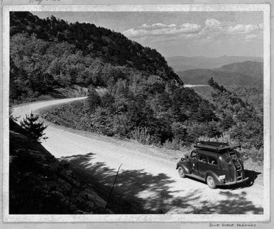A car drives along an unpaved portion of the Blue Ridge Parkway during the early years of construction.